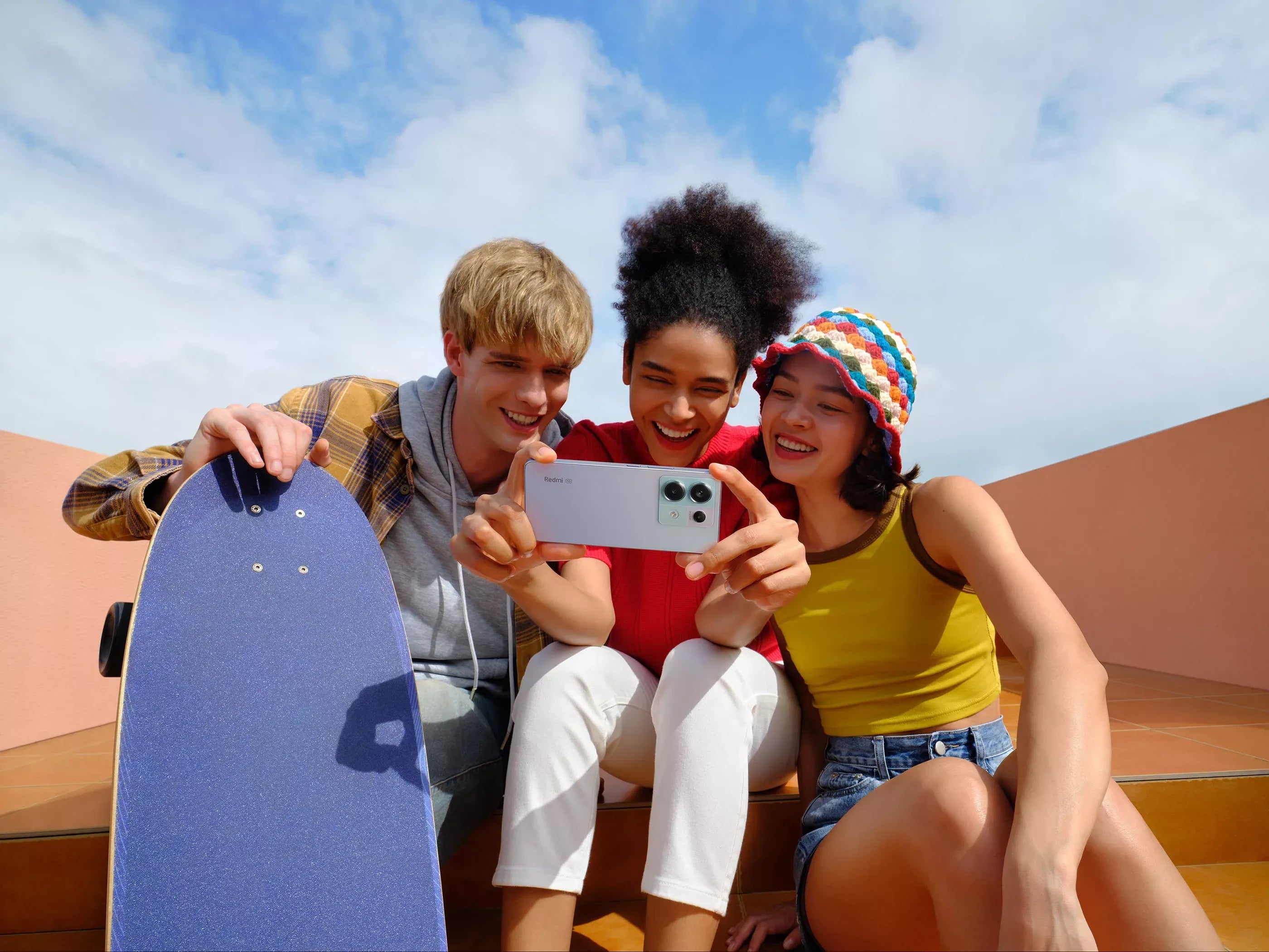 Three friends smiling and taking a selfie outdoors with a Redmi smartphone